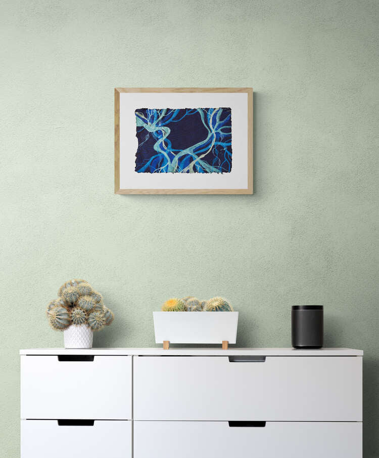 Painting on dark blue handmade paper, representing the seaweed Posidonia Oceanica, framed and hanging on a pale green wall above a white chest of drawers.