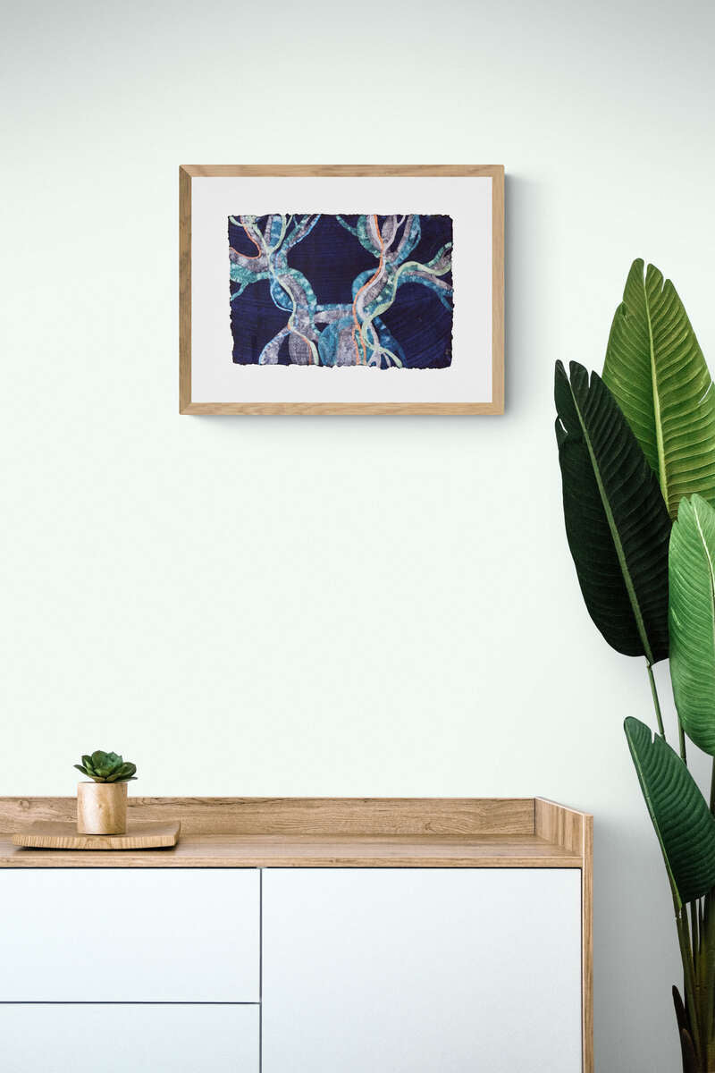 Painting representing Posidonia Oceanica with the colours of the Mediterranean sea glowing in the pale light of dawn, framed and hanging on a white wall, above a wood cabinet. 
